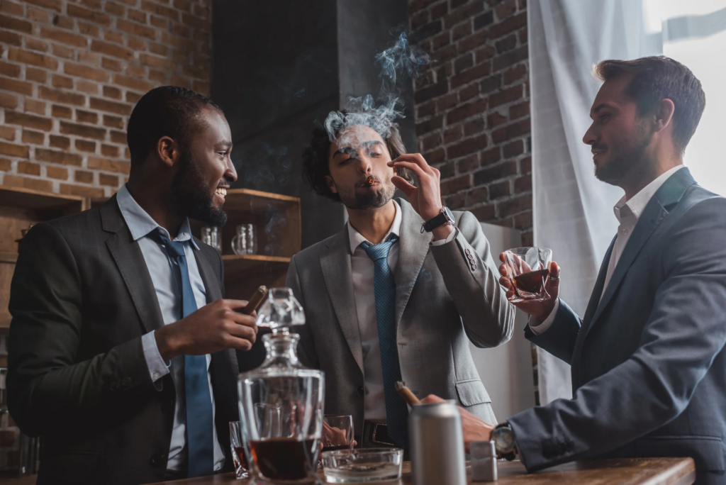 multiethnic male friends in suits smoking cigars, drinking whiskey and talking